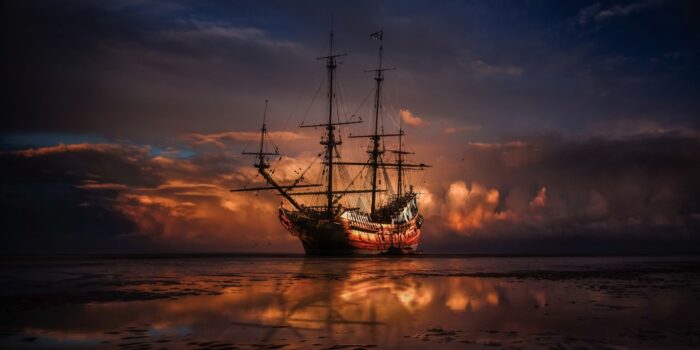 Ein historisches Segelschiff mit mehreren Masten, das bei Sonnenuntergang auf dem Wasser steht.