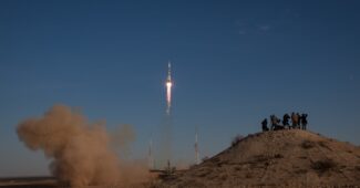 Eine Rakete startet vom Boden, während Zuschauer auf einem Hügel stehen und zuschauen.